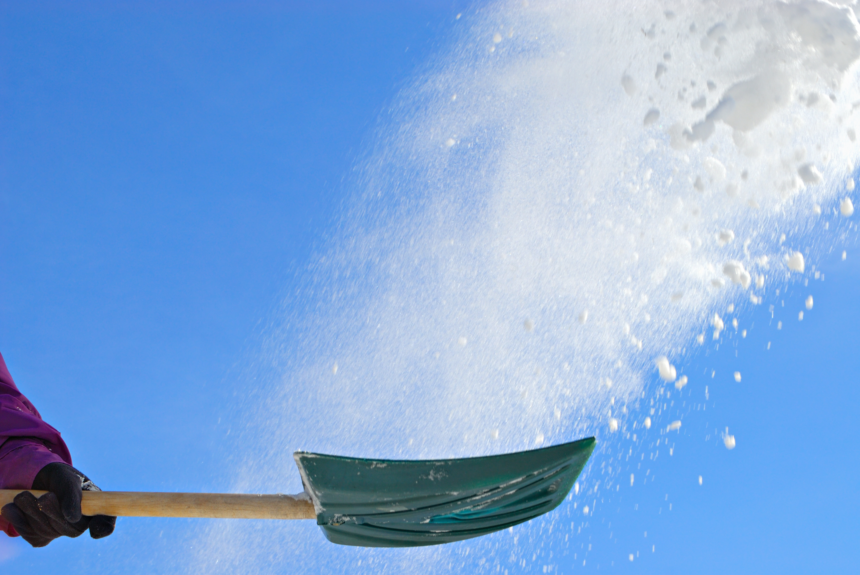 Snow shovel throwing snow in the air against blue sky